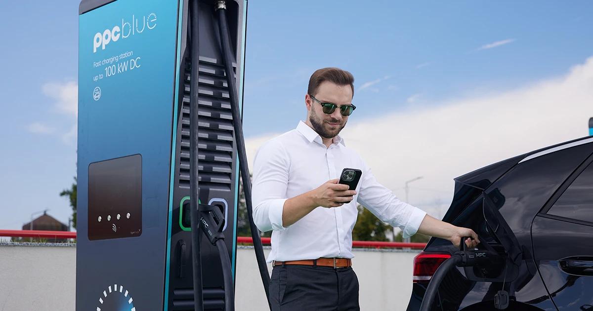 Bărbat care își încarcă vehiculul electric la o stație de încărcare PPC blue și care urmărește aplicația mobilă