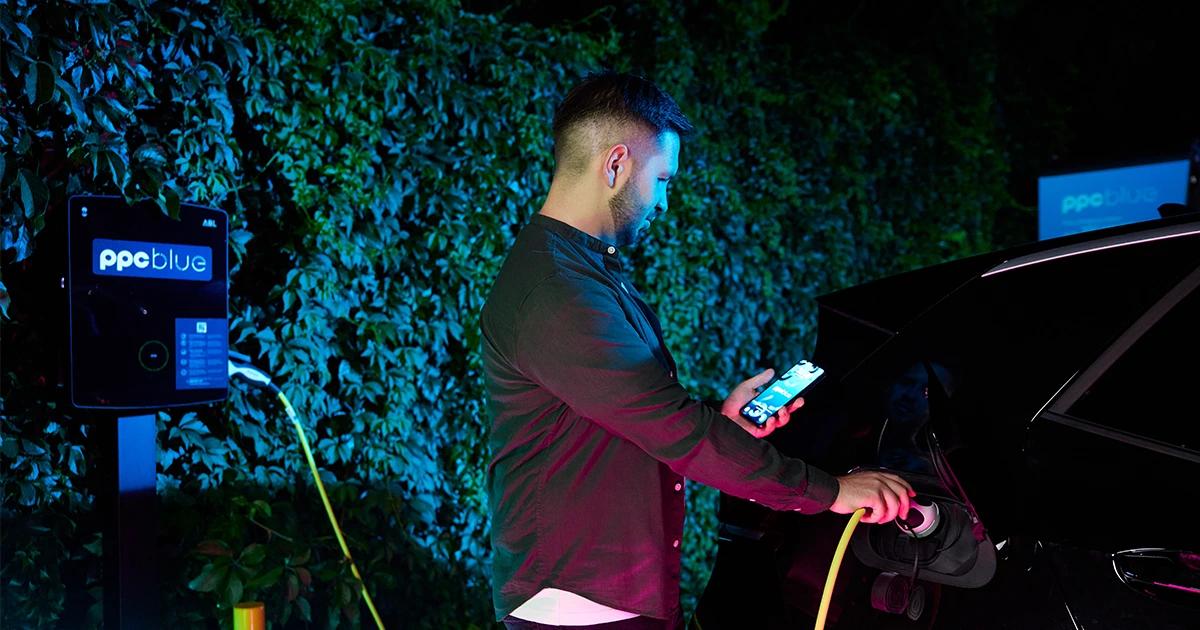 Bărbat care folosește aplicația PPC blue în timp ce încărcă mașina electrică